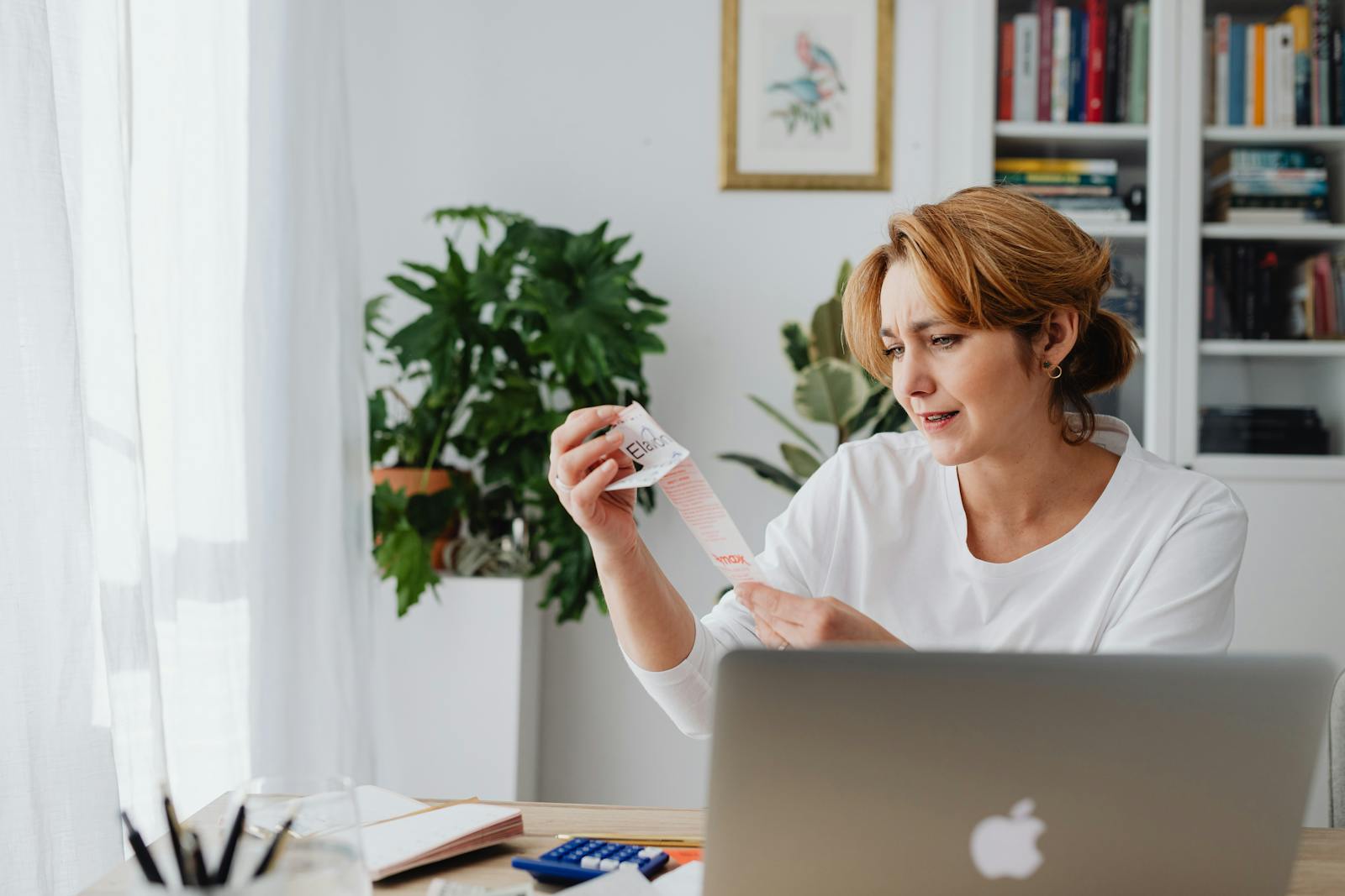 A woman reviewing expense receipts beside a laptop and calculator